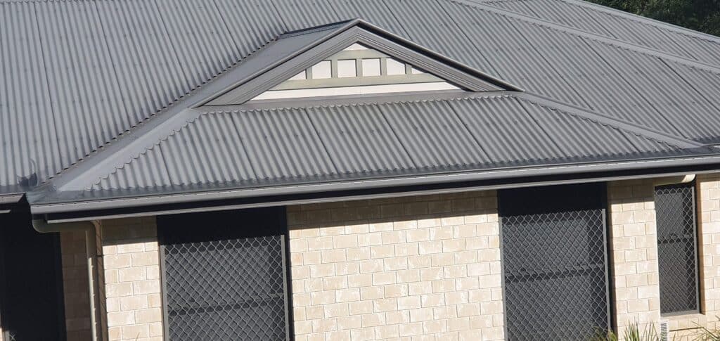 A brick house with a grey sheet roof with matching grey gutter mesh gutter guard.